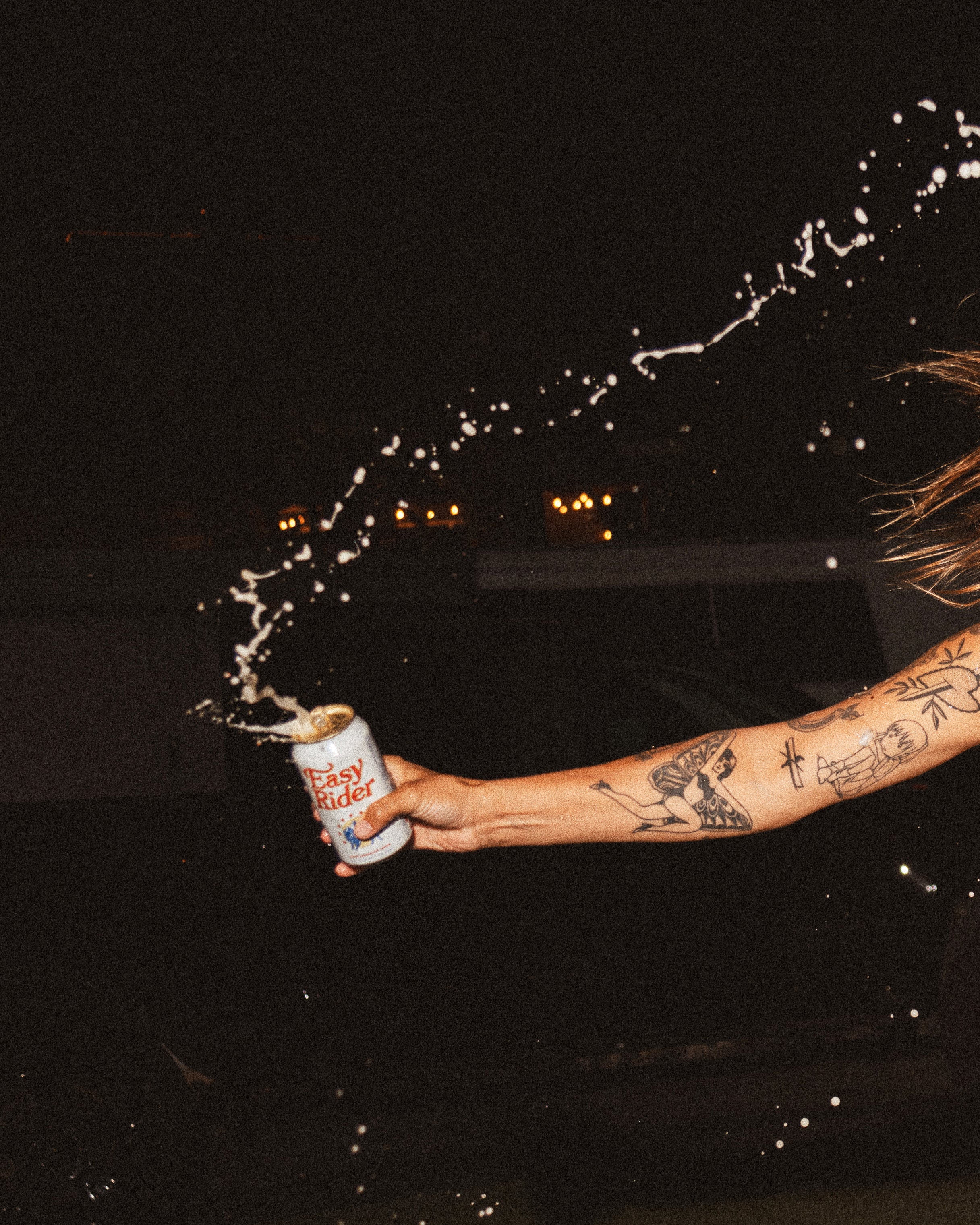 A tattooed arm swinging an open can of Easy Rider beer